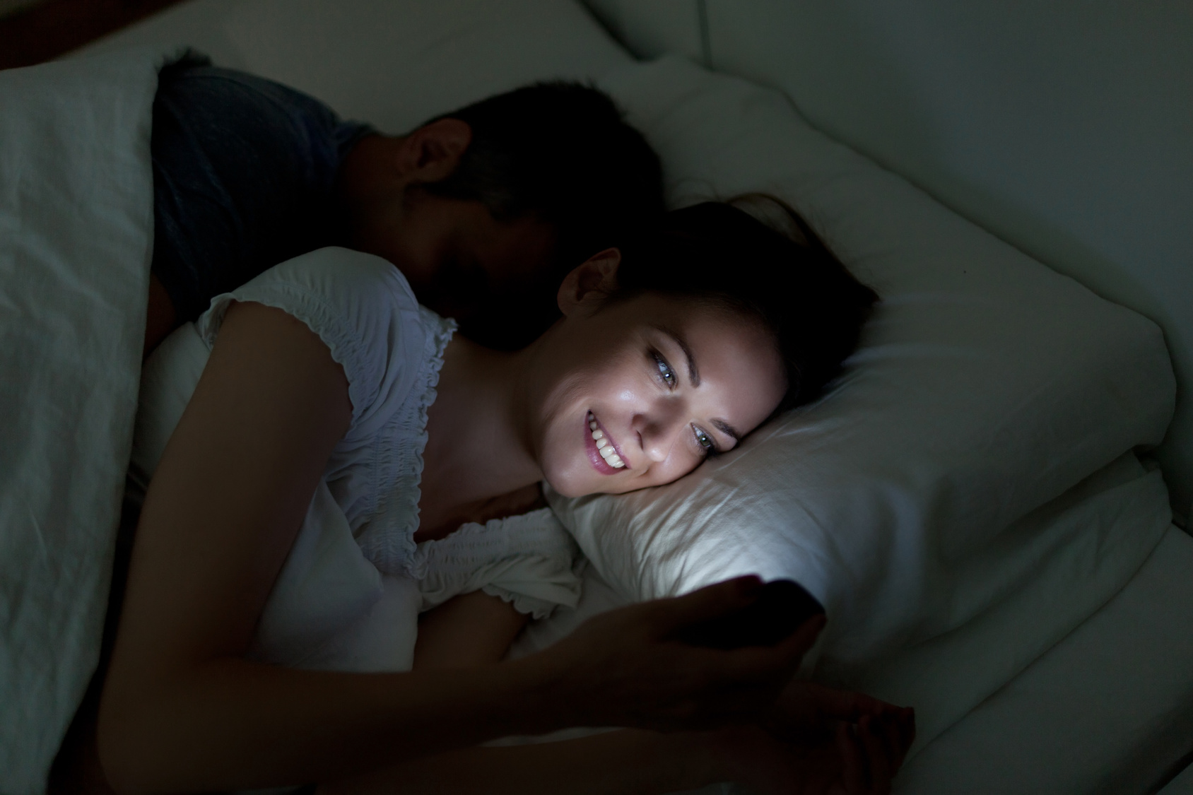 Young woman using mobile phone, while husband asleep