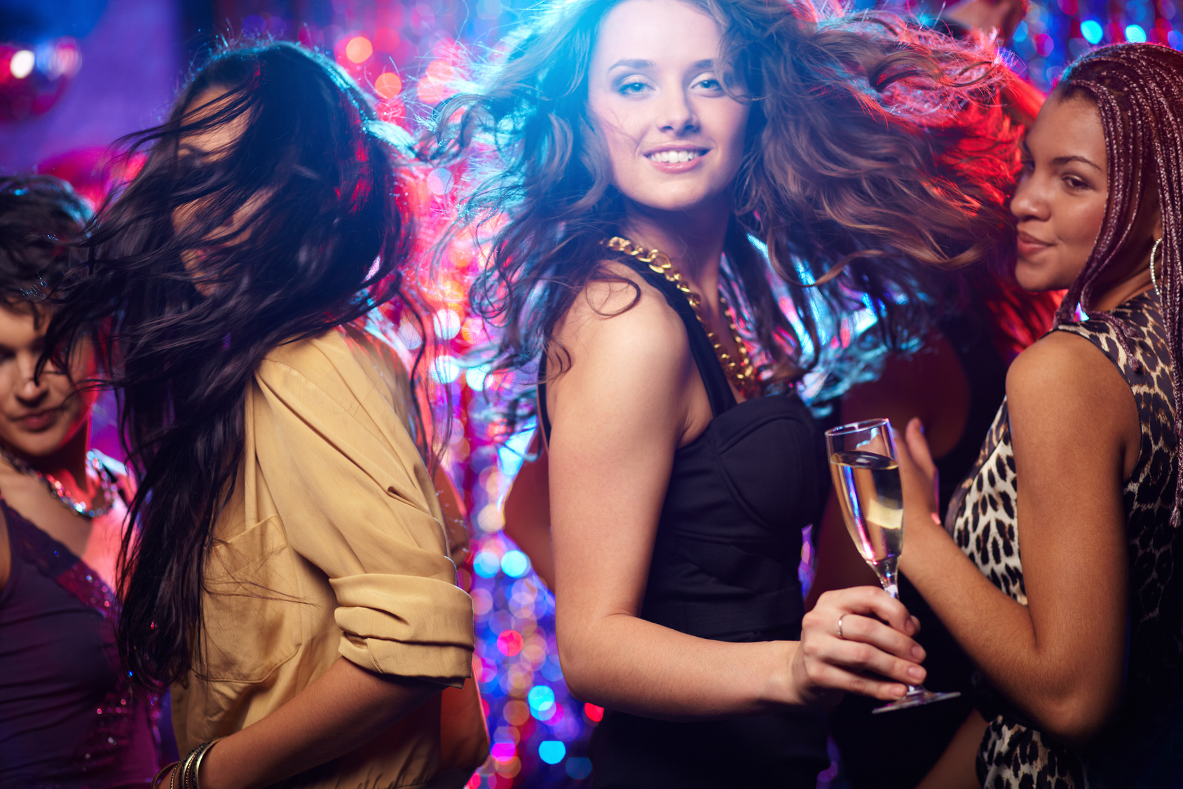Young woman looking at camera while dancing at nightclub among her friends