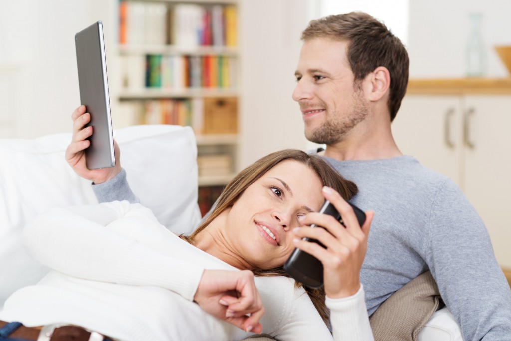 junges paar zuhause liest mit smartphone und tablet-pc
