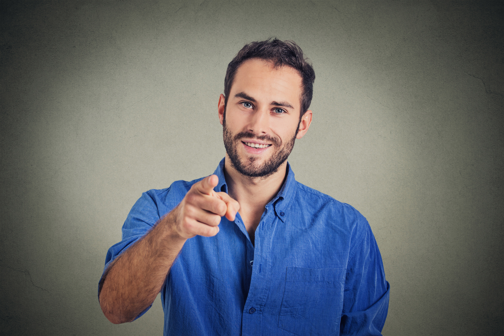 Handsome young man pointing finger at you isolated on gray wall background